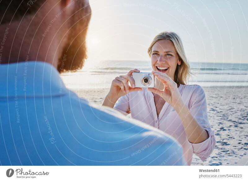 Happy woman taking a picture of man on the beach beaches photographing couple twosomes partnership couples camera cameras happiness happy people persons