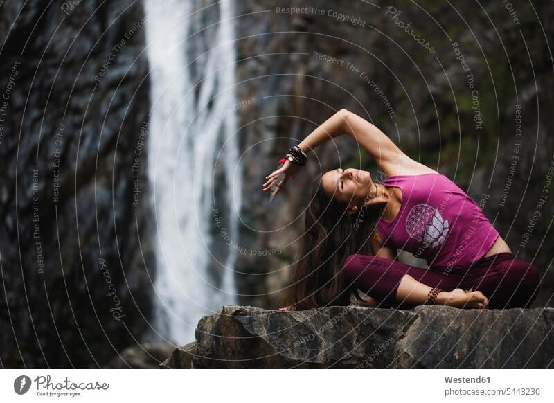 Italy, Lecco, woman doing yoga practice near a waterfall sitting Seated waterfalls females women mindfulness aware awareness self-care relaxation exercise
