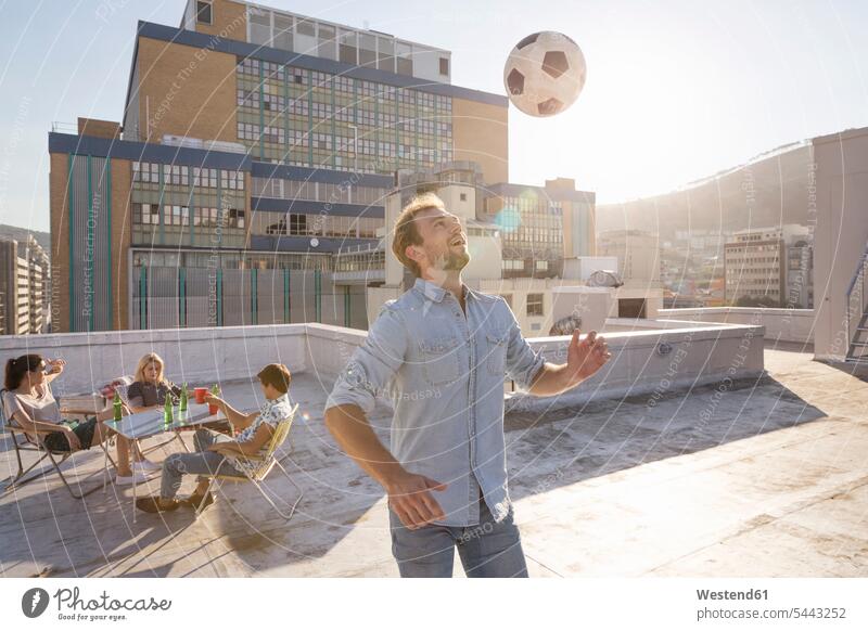 Friends meeting on rooftop terrace in summer, playing football friendship Quality Time active Encounter Meeting roof terrace deck togetherness carefree