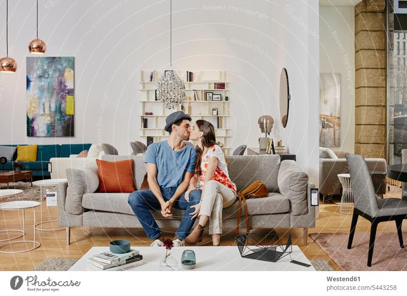 Couple in modern furniture store sitting on couch, kissing contemporary settee sofa sofas couches settees shopping hip trendy Seated couple twosomes partnership