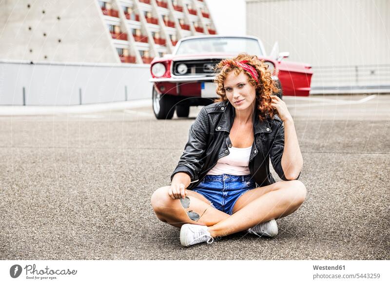 Portrait of confident redheaded woman sitting on parking level portrait portraits Seated car automobile Auto cars motorcars Automobiles females women