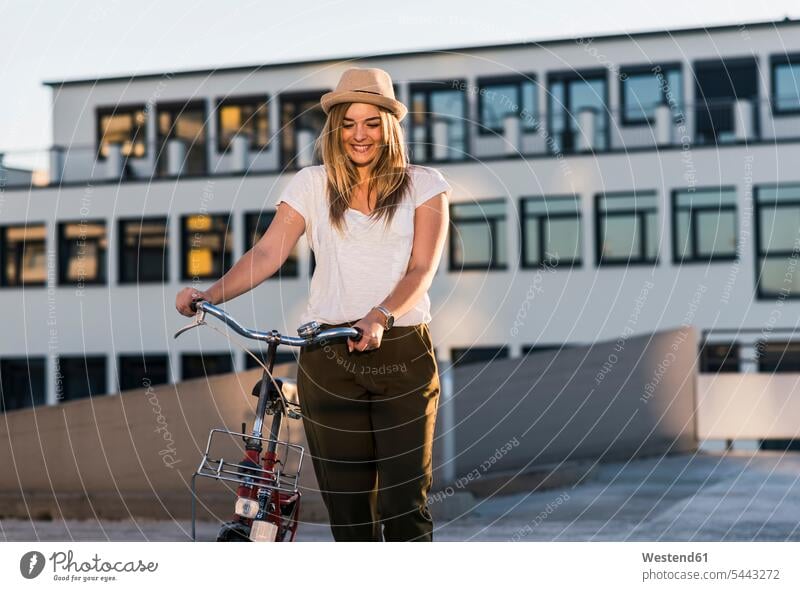 Smiling young woman with bicycle on parking level females women smiling smile bikes bicycles Adults grown-ups grownups adult people persons human being humans