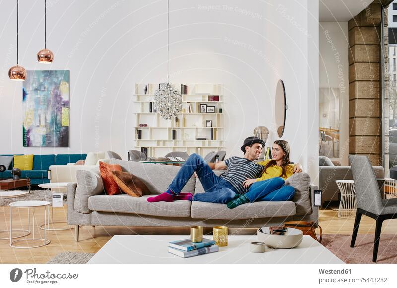 Couple in modern furniture store testing couch, being happy contemporary Furniture Furnitures hip trendy couple twosomes partnership couples sitting Seated