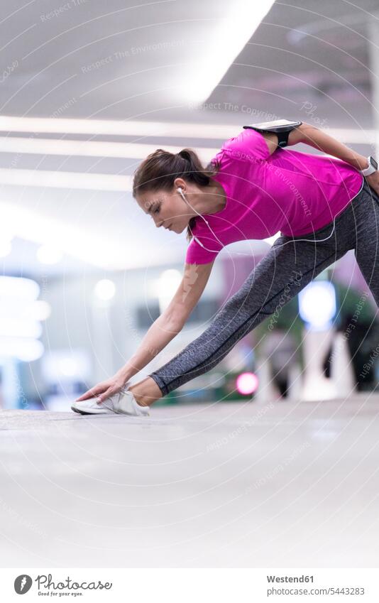 Young woman in pink sportshirt listening to music and stretching in front of modern building exercising exercise training practising young women young woman