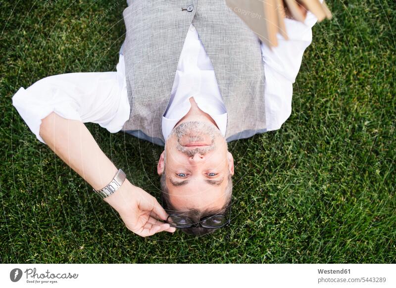 Mature businessman lying on grass meadow meadows laying down lie lying down men males relaxed relaxation break Adults grown-ups grownups adult people persons