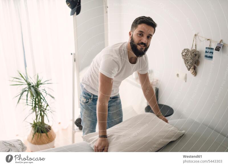 Young man making the bed at home smiling smile beds men males Adults grown-ups grownups adult people persons human being humans human beings Household Hipster
