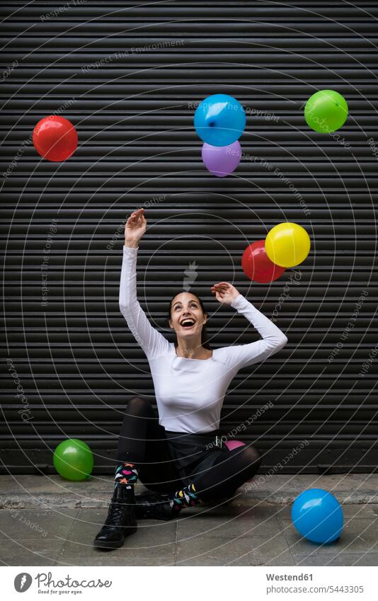 Laughing young woman sitting on pavement watching flying balloons females women laughing Laughter Adults grown-ups grownups adult people persons human being