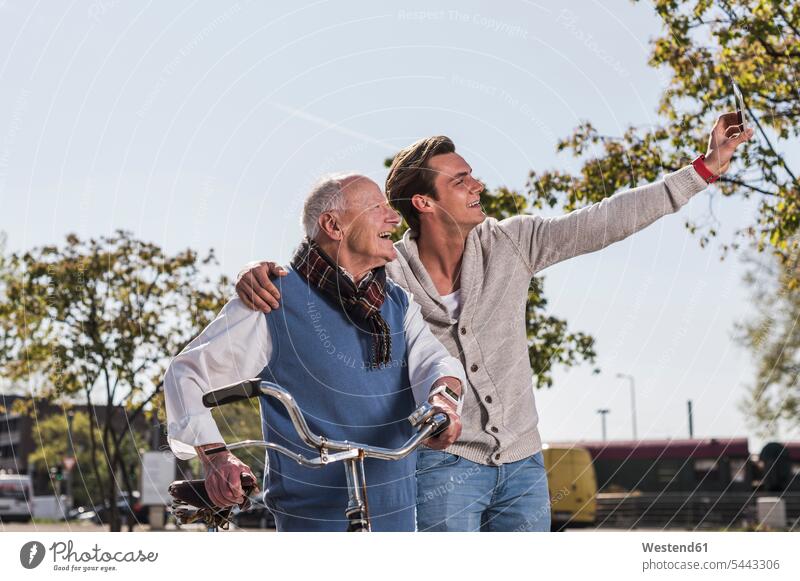 Senior man and adult grandson taking a selfie outdoors Fun having fun funny smiling smile mobile phone mobiles mobile phones Cellphone cell phone cell phones