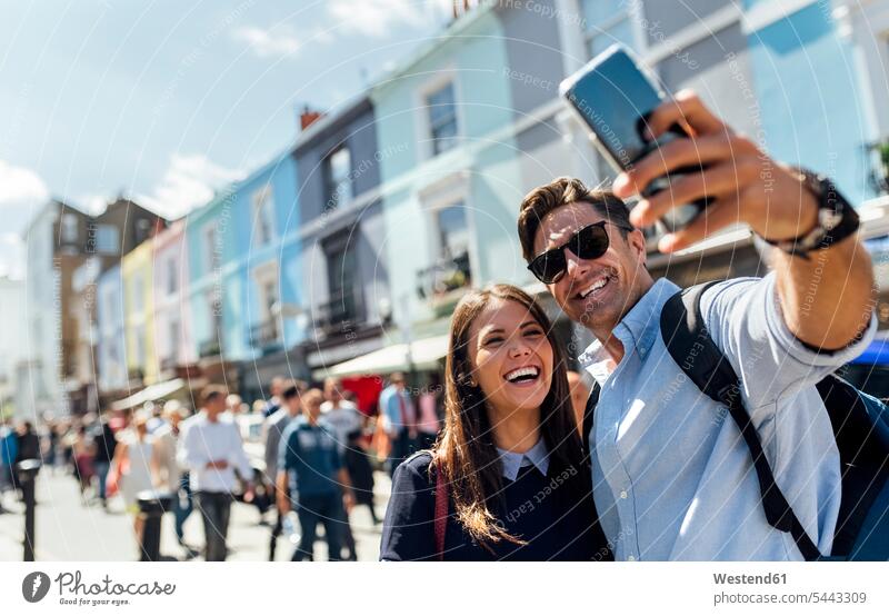 UK, London, Portobello Road, portrait of laughing couple taking selfie with smartphone portraits twosomes partnership couples Selfie Selfies people persons