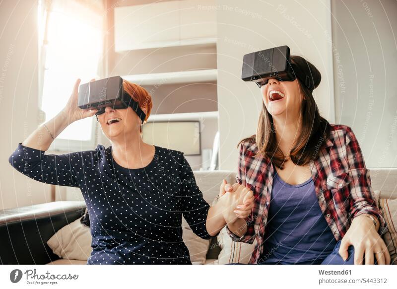 Excited adult daughter with mother at home wearing VR glasses virtual happiness happy woman females women laughing Laughter mommy mothers mummy mama daughters