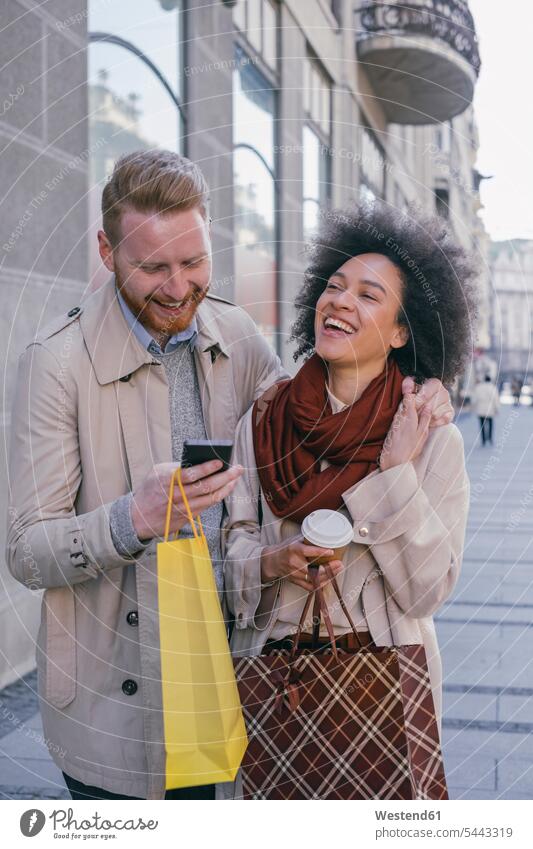 Happy couple in the city with cell phone and shopping bags twosomes partnership couples laughing Laughter mobile phone mobiles mobile phones Cellphone