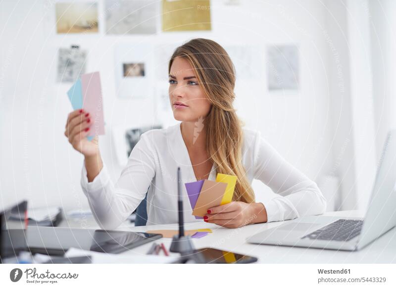 Young woman looking at notes at desk in office slip memo notice working At Work offices office room office rooms workplace work place place of work desks