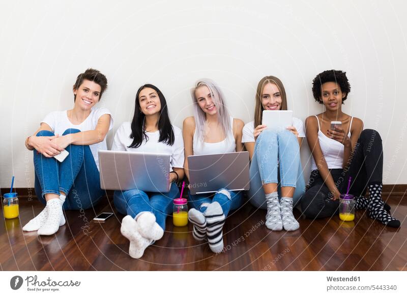 Portrait of smiling female friends at home sitting on floor using technology Smartphone iPhone Smartphones laptop Laptop Computers laptops notebook smile