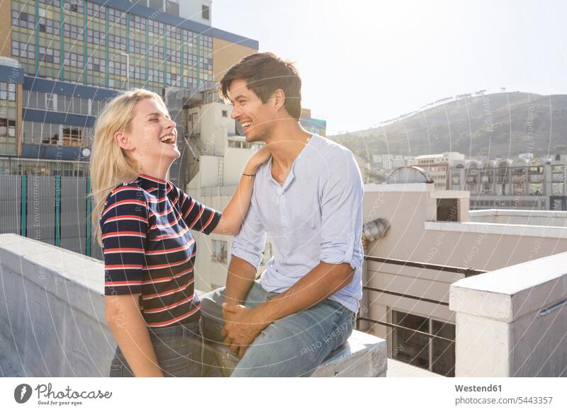 Young couple flirting on a rooftop terrace Flirtation laughing Laughter twosomes partnership couples meeting encounter gathering carefree friends together