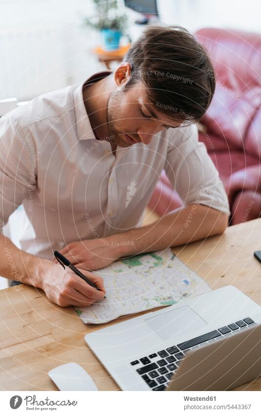 Young man with city map and laptop at home men males Adults grown-ups grownups adult people persons human being humans human beings sitting Seated