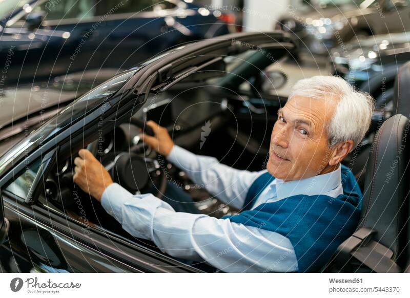 Senior man testing convertible in car dealership automobile Auto cars motorcars Automobiles car dealerships buying customer clientele clients customers choosing
