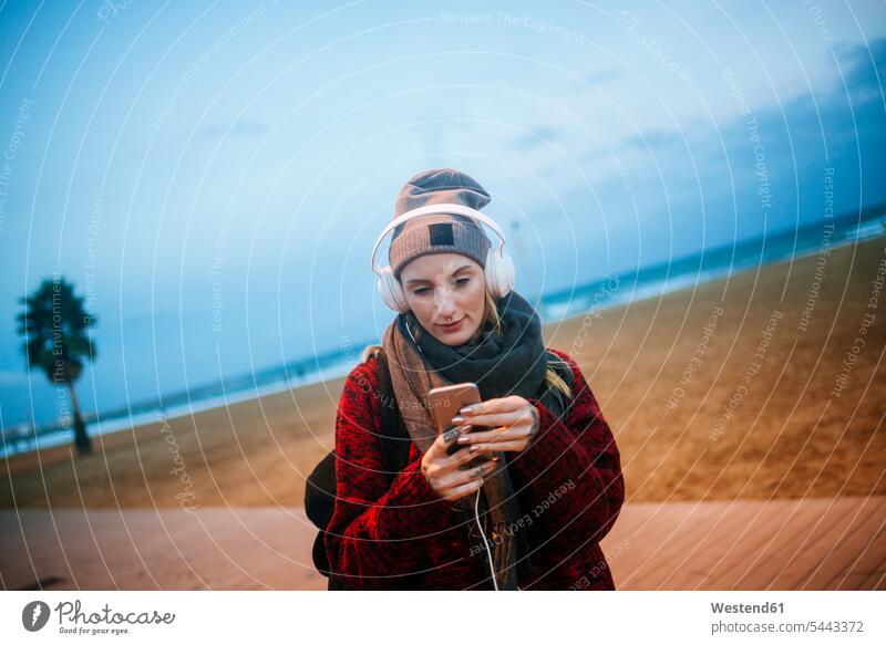 Young woman listening to music on a smartphone on the beach at dusk mobile phone mobiles mobile phones Cellphone cell phone cell phones females women headphones