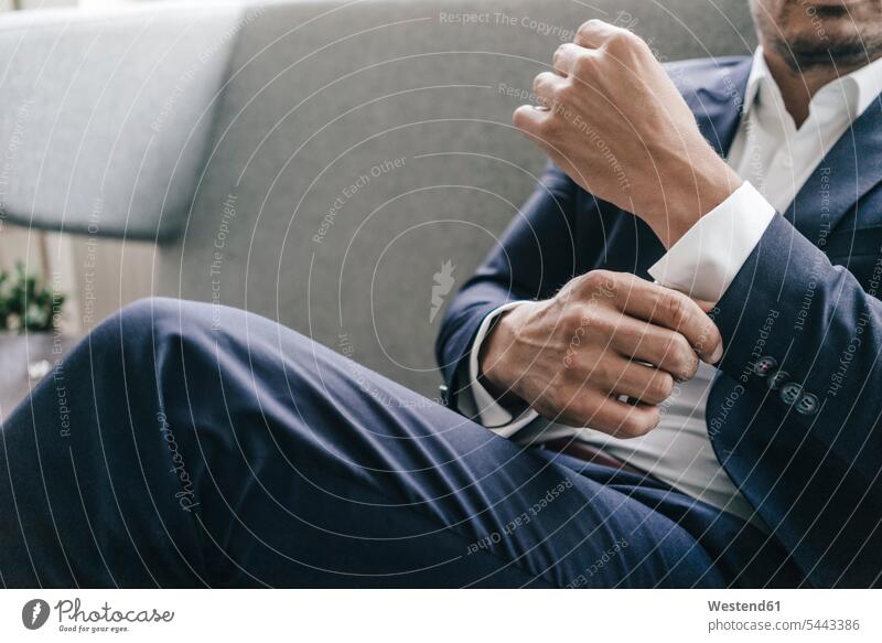 Close-up of businessman adjusting his sleeves men males couch settee sofa sofas couches settees Businessman Business man Businessmen Business men sitting Seated