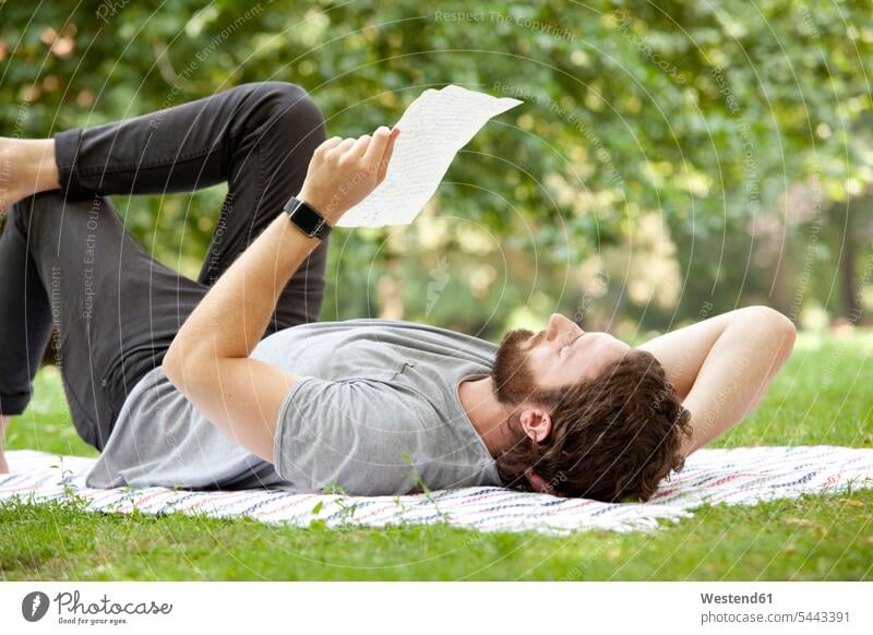 Man lying on blanket in a park reading a letter letter document letters man males mail post Adults grown-ups grownups adult people persons human being humans