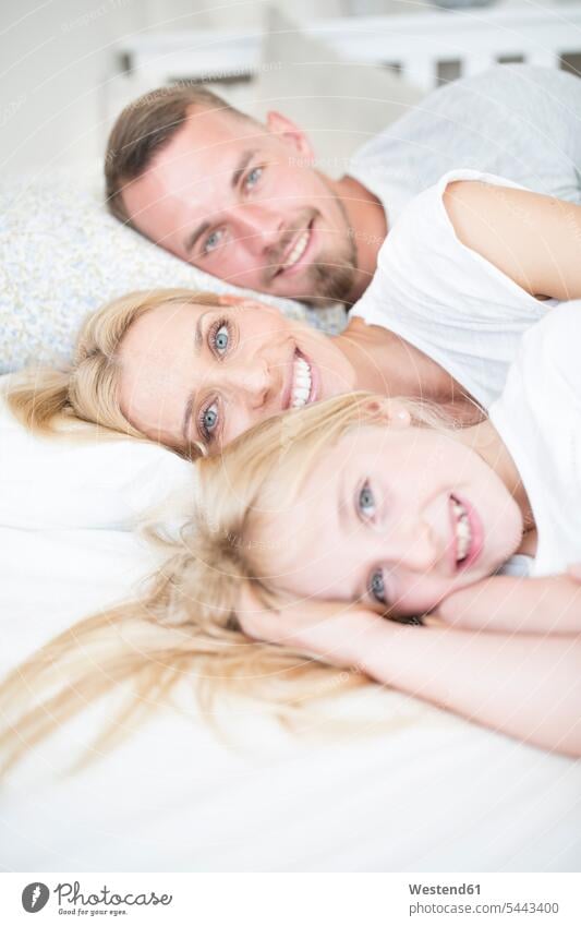 Portait of smiling girl and parents lying in bed laying down lie lying down daughter daughters smile beds family families child children people persons