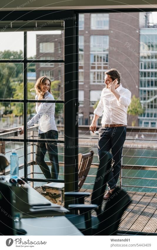 Businessman and woman standing on balcony, man making a phone call independence independent mobile phone mobiles mobile phones Cellphone cell phone cell phones