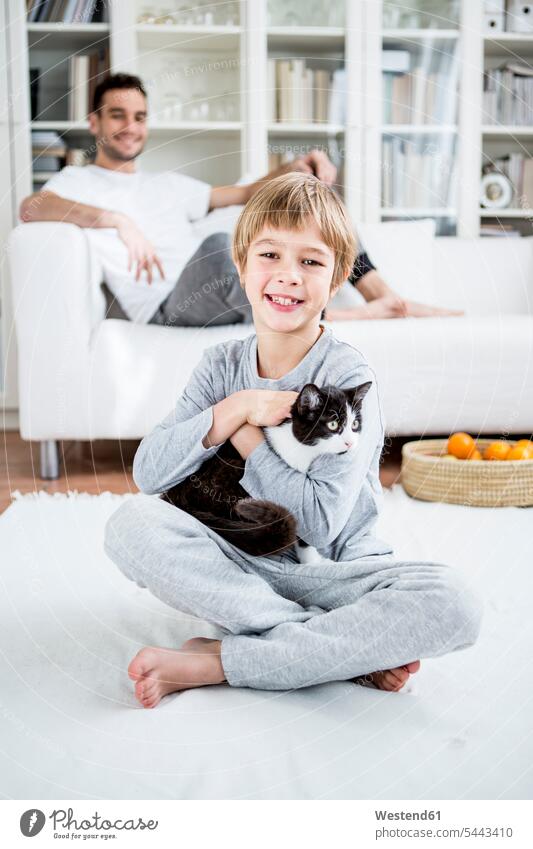 Smiling boy caressing cat at home cats son sons manchild manchildren smiling smile boys males family families pets animal creatures animals people persons