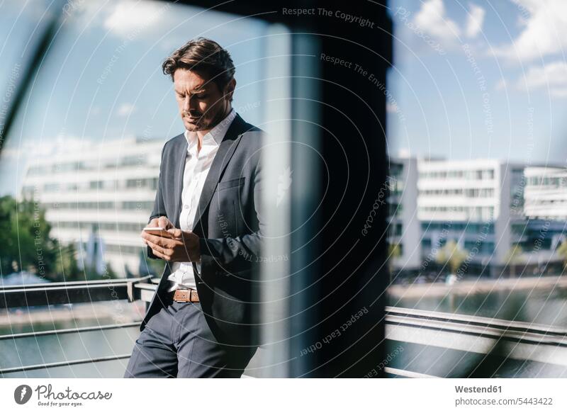 Businessman standing on balcony, holding smartphone mobile phone mobiles mobile phones Cellphone cell phone cell phones balconies Business man Businessmen