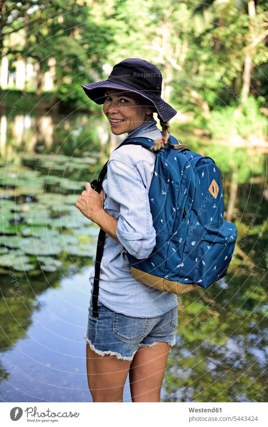 Portrait of smiling woman with backpack standing in front of a lake females women rucksacks backpacks back-packs portrait portraits Adults grown-ups grownups