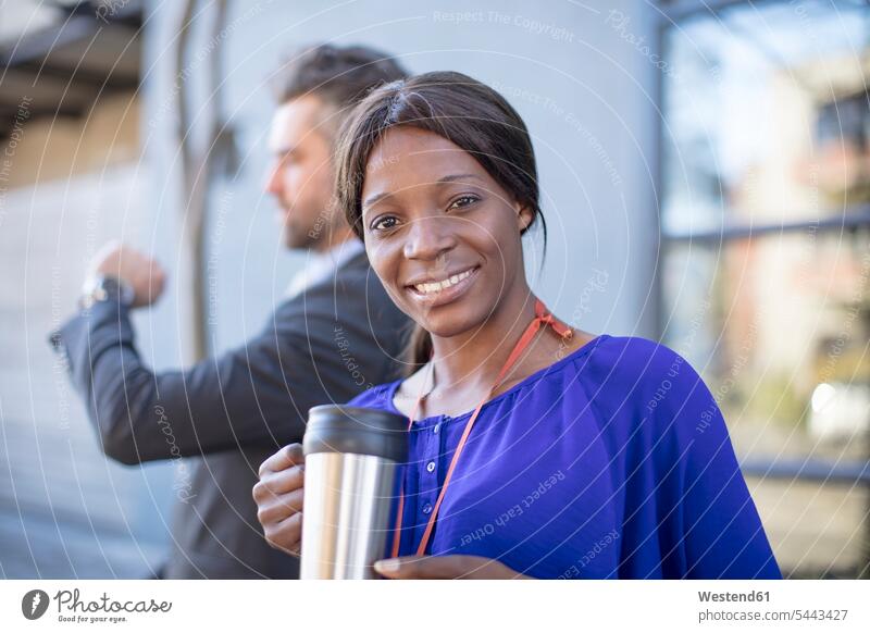 Portrait of smiling businesswoman with coffee mug and businessman in background businesswomen business woman business women Coffee portrait portraits smile