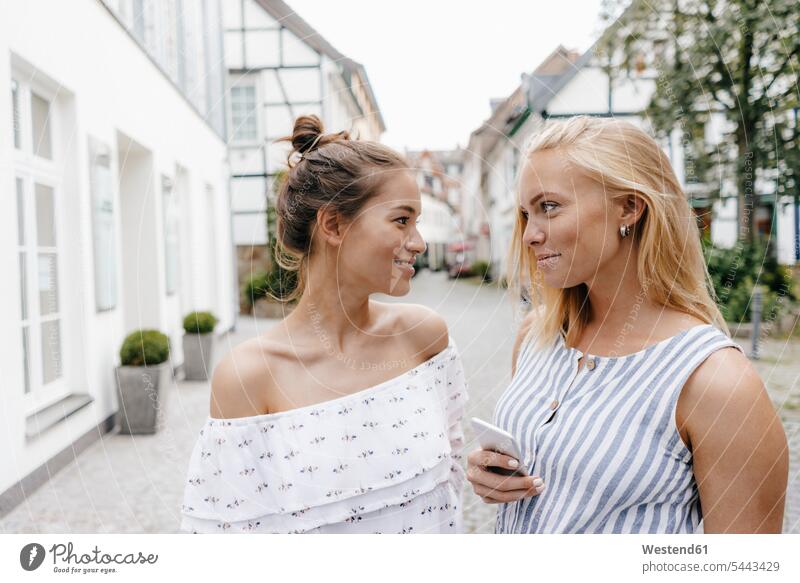 Two smiling young women looking at each other in the city female friends eyeing woman females town cities towns smile mate friendship view seeing viewing Adults