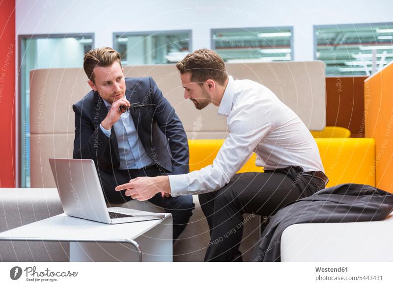 Businessmen sitting in conversation pit, discussing in front of laptop colleagues Seated using laptop using a laptop Using Laptops discussion work meeting