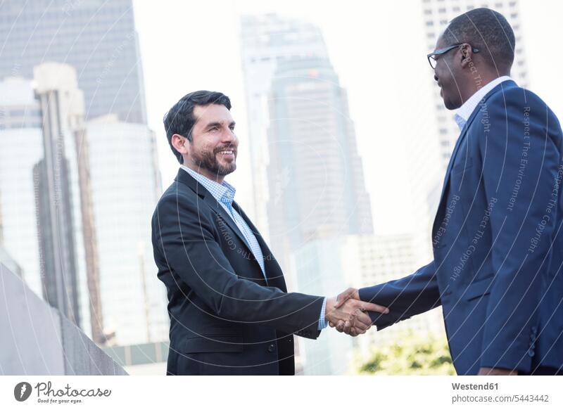 Two businessmen shaking hands in the city Handclasp Handclap Businessman Business man Businessmen Business men smiling smile colleagues handshake