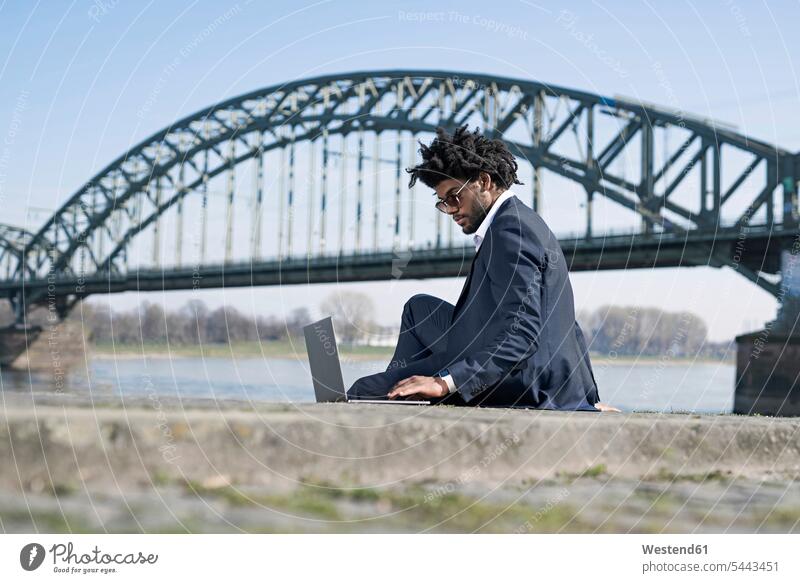 Businessman sitting at the riverside using laptop Business man Businessmen Business men Laptop Computers laptops notebook males business people businesspeople