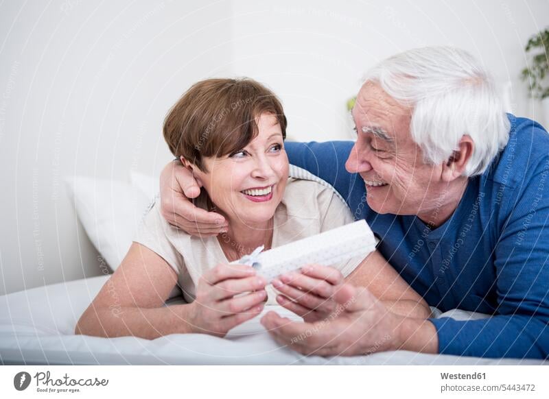 Senior couple lying in bed, man giving present to woman caucasian caucasian ethnicity caucasian appearance european bonding carefree beds relationship