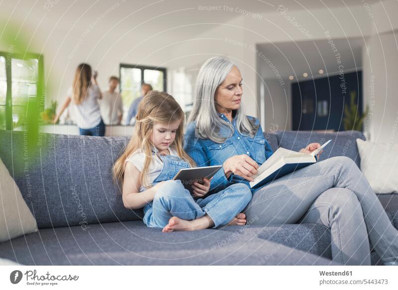 Grandmother and granddaughter sitting on couch, reading together book and tablet pc books learning settee sofa sofas couches settees granddaughters digitizer