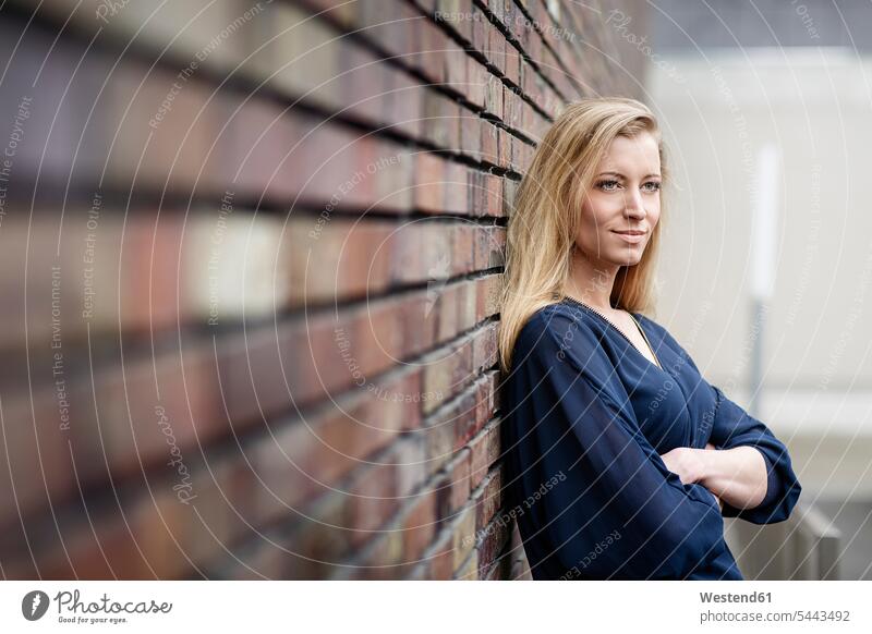 Portrait of smiling blond young woman leaning against brick wall females women portrait portraits Adults grown-ups grownups adult people persons human being