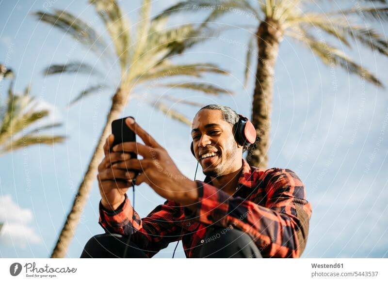 Spain, portrait of smiling young man listening music with headphones looking at cell phone headset men males Adults grown-ups grownups adult people persons