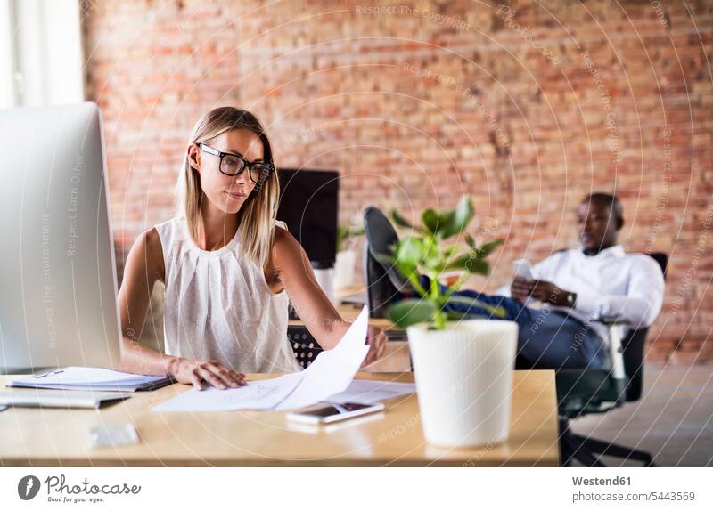Businesswoman working at desk in office with colleague in background At Work sitting Seated businesswoman businesswomen business woman business women offices