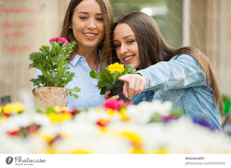 Girlfriends choosing potted plants at flower stall pointing point at pointing at show showing gardening yardwork yard work pot  plants pot plant looking eyeing