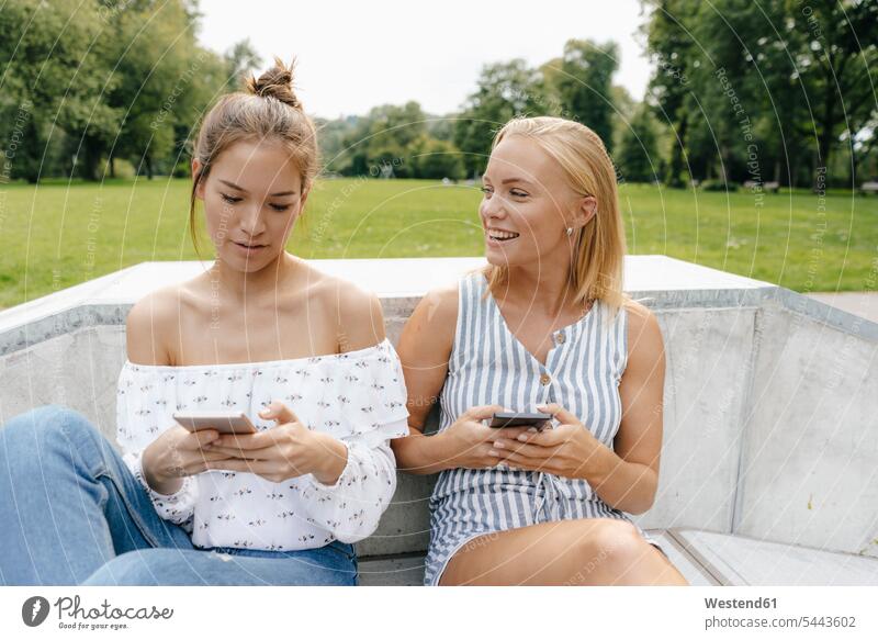 Two happy young women with cell phones in a skatepark female friends Skateboard Park skate park parks happiness woman females mobile phone mobiles mobile phones