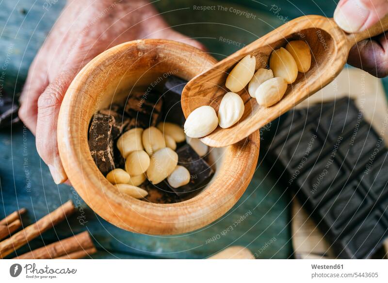 Man's hands pouring almonds in a wooden bowl with chocolate man men males Chocolate Chocolates human hand human hands Adults grown-ups grownups adult people