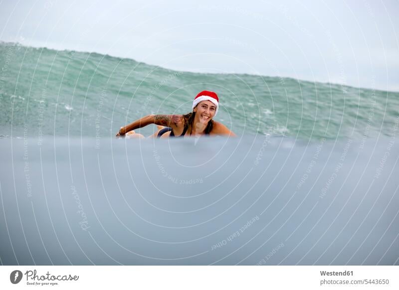 Indonesia, Bali, smiling woman on surfboard wearing Santa hat surfboards smile wave waves Sea ocean surfing surf ride surf riding Surfboarding females women