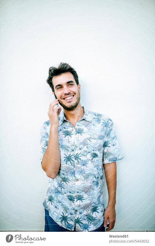 Man on cell phone in front of white wall Smartphone iPhone Smartphones on the phone call telephoning On The Telephone calling smiling smile man men males
