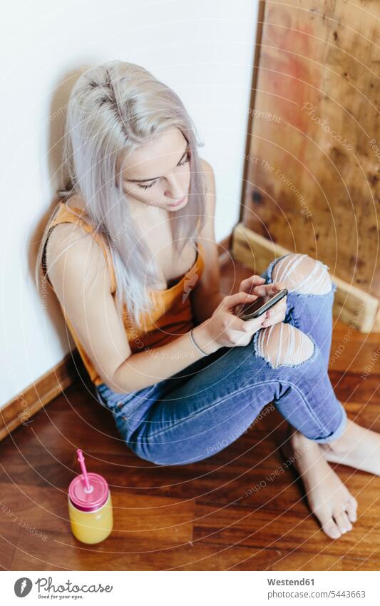 Young woman sitting on the floor at home using smartphone use Seated females women floors Smartphone iPhone Smartphones Adults grown-ups grownups adult people