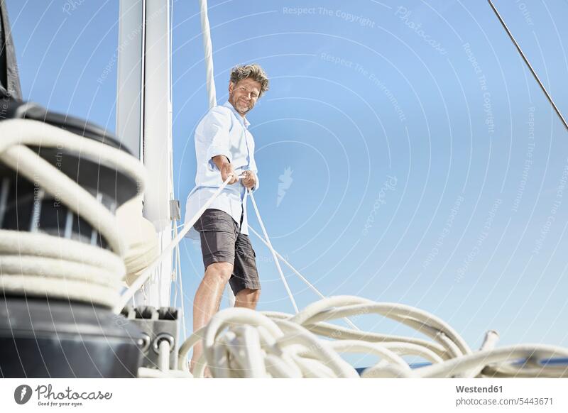 Smiling mature man working with ropes on sailing boat men males Adults grown-ups grownups adult people persons human being humans human beings boat sports Sea