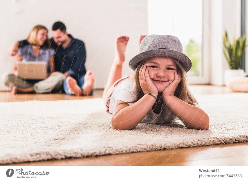 Little girl with hat having fun at home, parents using laptop in background Germany Quality Time togetherness wireless Wireless Connection Wireless Technology