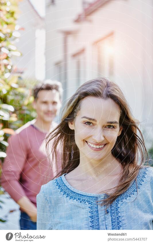 Portrait of smiling woman with man in background couple twosomes partnership couples home ownership private owned home portrait portraits smile people persons