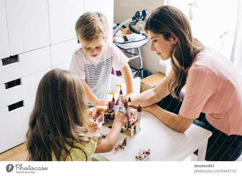 Mother with two children building up toy castle at home setting up build up set up family families playing mother mommy mothers ma mummy mama people persons