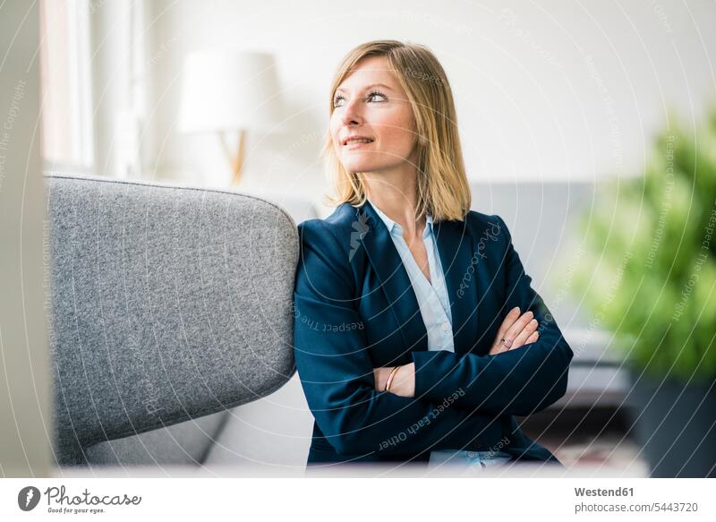 Smiling businesswoman sitting on couch in office lounge Seated offices office room office rooms lounges Lounge Room smiling smile businesswomen business woman