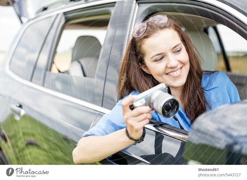 Woman sitting in car holding camera woman females women car driving motoring automobile Auto cars motorcars Automobiles Road Trip roadtrip Road-Trip Adults